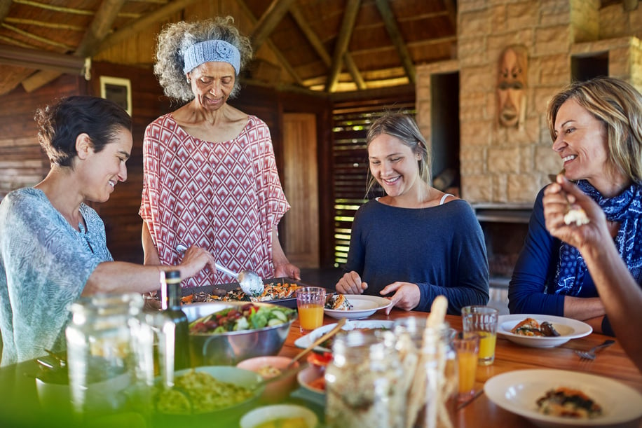 Friends enjoying healthy meal in hut during yoga retreat.